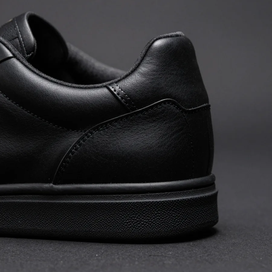 Close macro detail of the material and construction of a black leather low-top sneaker with a tonal P monogram quarter panel.