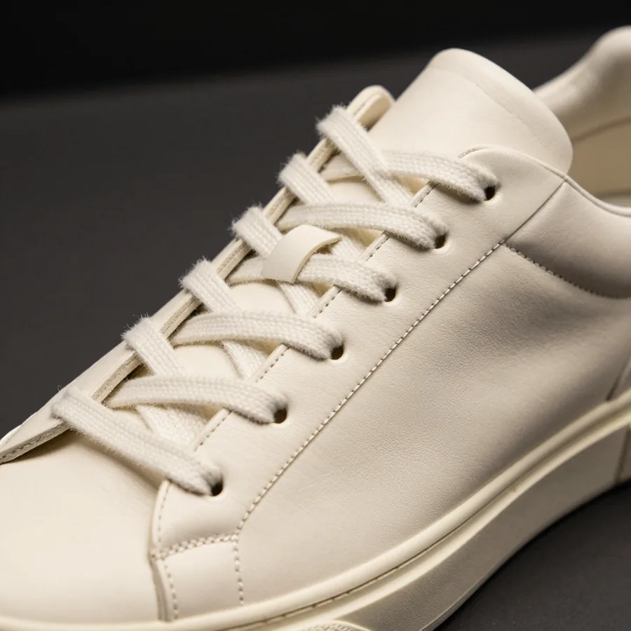 Close macro detail of the material and construction of a bone ivory leather low-top sneaker with a thin structured sole.