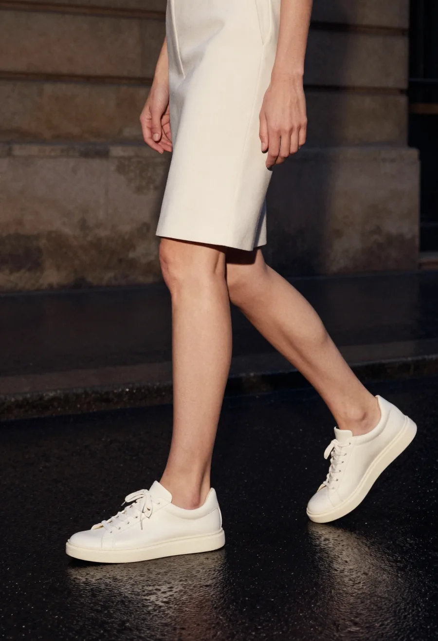 A model wearing a bone ivory leather low-top sneaker with a thin structured sole on a wet Paris street at night.