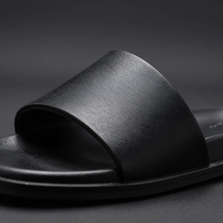 Close macro detail of the material and construction of a black leather slide sandal with the P embossed into its single wide strap.