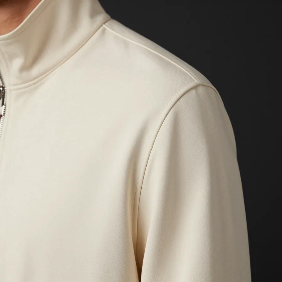 Close macro detail of the material and construction of a bone ivory tailored track jacket with a structured shoulder and a P emblem at the chest.