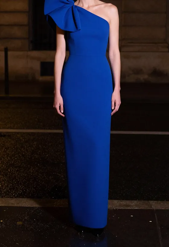 A model facing the camera, wearing a cobalt column gown with one structured sculptural shoulder, on a wet Paris street at night.