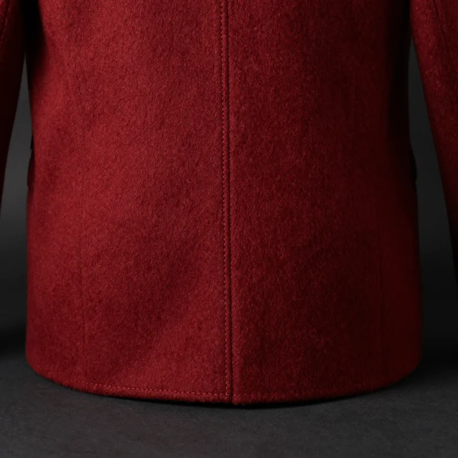 Close macro detail of the seam construction of a floor-brushing oxblood wool overcoat with the trademark house seam running the full front panel.