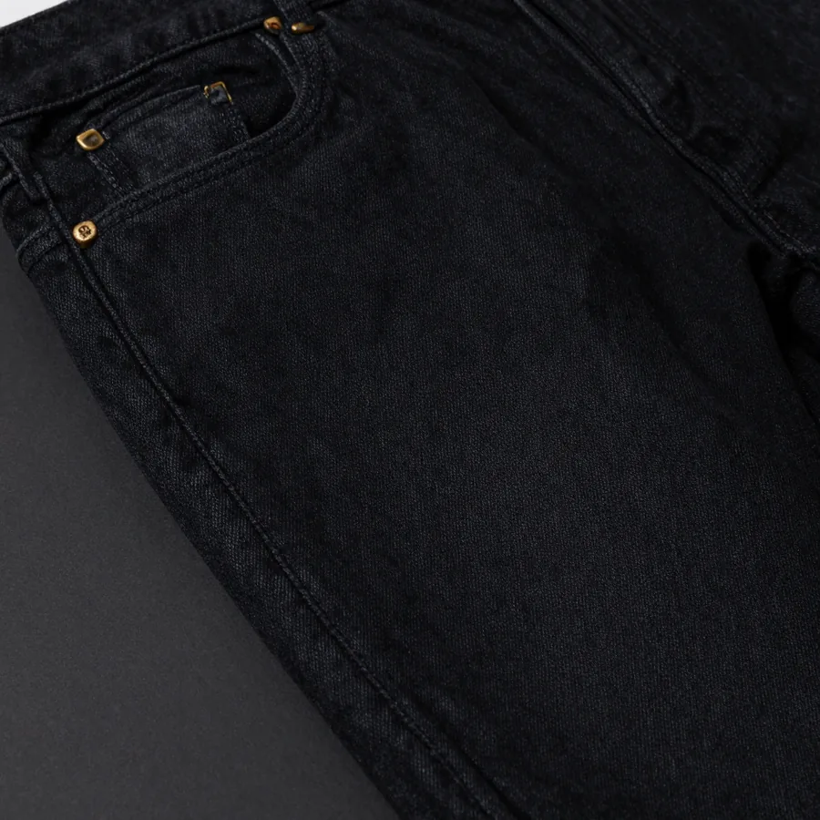 Close macro detail of the seam construction of a pair of black rinse straight-leg jeans whose trademark house seam runs the outseam with a curved hip yoke.